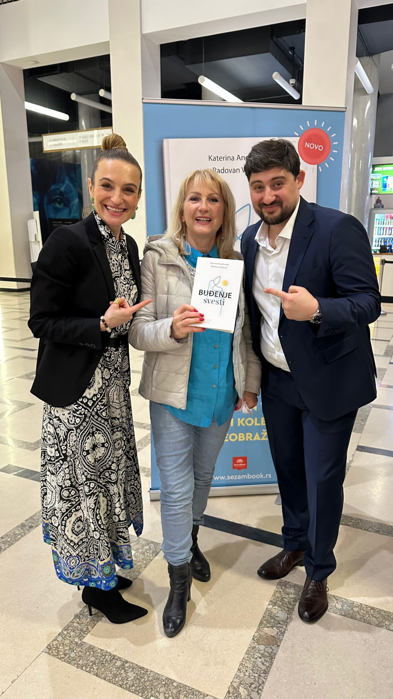 Readers holding a copy of Buđenje svesti at the Belgrade promotion, 2023, beside the title banner